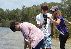 students stand in the lake to learn how to use the water-quality meter