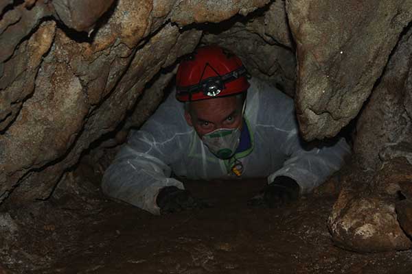 Professor Hamish McGowan wearing a headlamp crawling through a small cave to gain access to stalagmites around 120 metres below the surface in the Grotto Cave, NSW.
