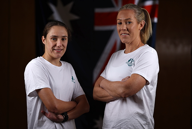 Two women wearing white Commonwealth Games t-shirts. The women are angled towards each other with their arms crossed.