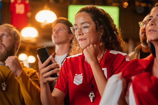  A woman cheering while streaming a sports event on her phone. She is wearing her team's football jersey.