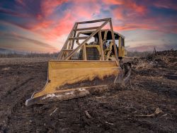 Bulldozer sitting on cleared land under pink sky. Adobe