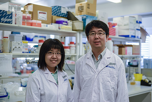 Two scientists wearing lab coats in a science laboratory. They are both smiling.