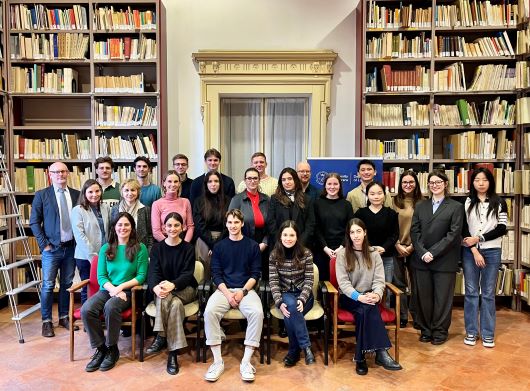 A group of students stand in a library full of books.