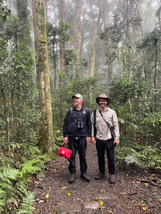 Two men dressed in long sleeved shirts, pants and hats in the rainforest
