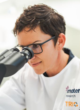 A female scientist in a white lab coast looks through a microscope.