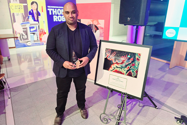 Associate Professor Arutha Kulasinghe with his award standing next to his digital image of a skin cancer.