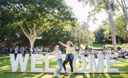 Students at UQ in front of a Welcome sign.