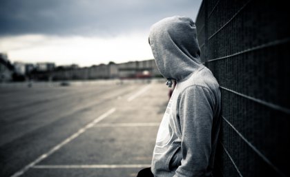 A teenager wearing a hoodie leans against a wall.