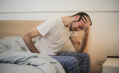 Man sitting on side of bed with head in his hands.