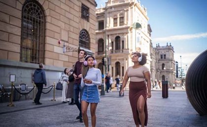 Three people standing in the middle of a city wearing headphones and looking up