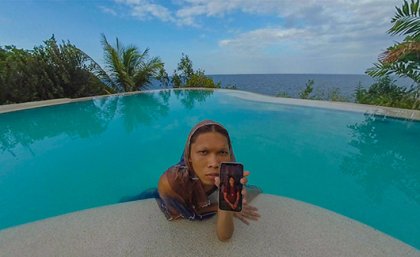 A woman leaning onto the edge of a swimming pool, holding a mobile phone 