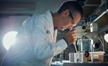 Uno scienziato in camice e occhiali protettivi tiene una pipetta sopra un grande ragno nero in un contenitore.