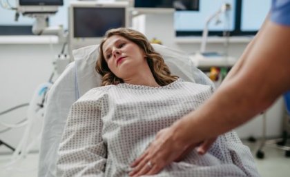 Woman in hospital bed wearing a hospital gown with her abdomen being examined. 