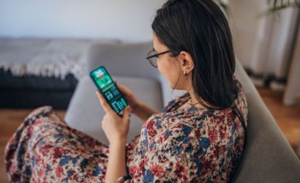 A woman sits on a couch looking at a phone showing a sports betting app