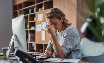 A woman in a grey sweater looking frustratingly at her computer 