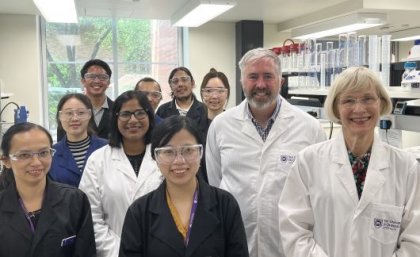 A group of people standing in a laboratory wearing white lab coats.