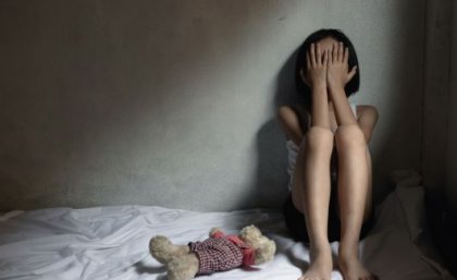 A young child sitting on a bed with their head in their hands, looking upset