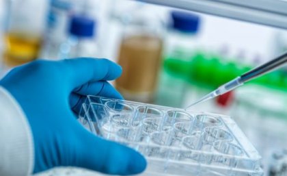 A gloved hand holds a tray of vials as a pipette hovers in a laboratory setting.