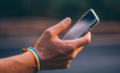 Image: Adobe. A hand wearing a rainbow bracelet holds a mobile phone.