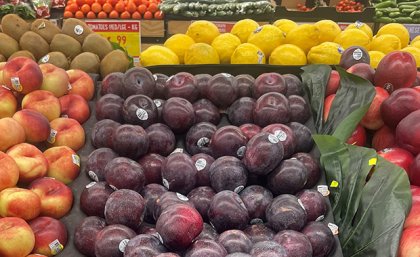 a tray of plums among other fruit in a supermarket
