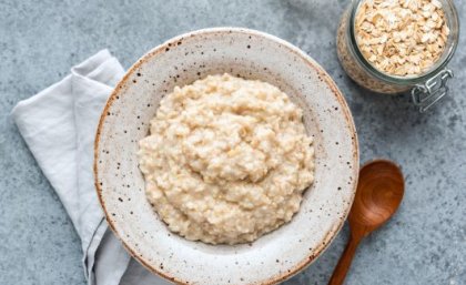 Image: Adobe. a bowl of porridge sits next to a wooden spoon and a jar of uncooked oats