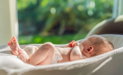 Image, Adobe. Newborn baby lying on bed in the sunlight.