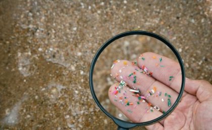 Microplastics in the environment can have adverse impacts on environmental and human health. Image: Adobe. Fingers holding microplastics shown through a magnifying glass