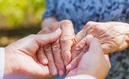 Image: Adobe. A person clasps hands with an elderly person