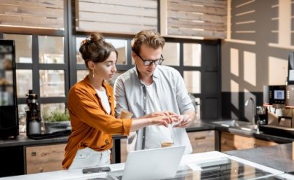 Image: Adobe. A man and woman in a workplace stand next to a laptop