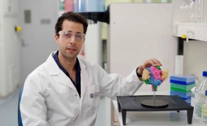 a man in a white lab coat sits next to a multicoloured model