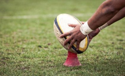 Image: Adobe. Hands holding a rugby ball on a kicking tee.
