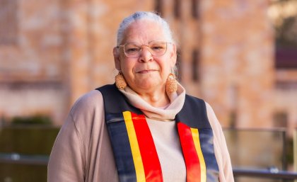 Aunty Jacqueline Kina at UQ's Aboriginal and Torres Strait Islander Sashing Ceremony. Aunty Jacqueline Kina standing in front of a sandstone building.