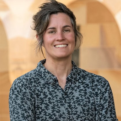 Professor Felicity Meakins A woman in a patterned grey and black shirt standing in front of a sandstone building