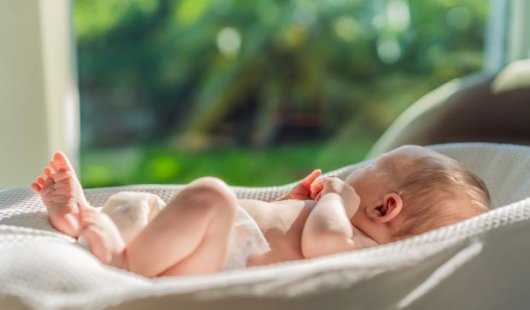 Newborn baby lying on bed in the sunlight.