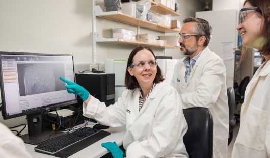 Three scientists in white lab coats looking at a computer screen.