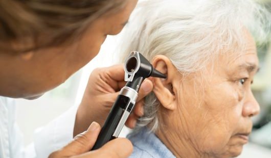 A audiologist inserting a stethoscope into a elderly patient's ear