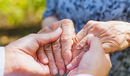A person clasps hands with an elderly person