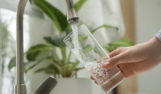 Person filling glass with water from tap. Adobe