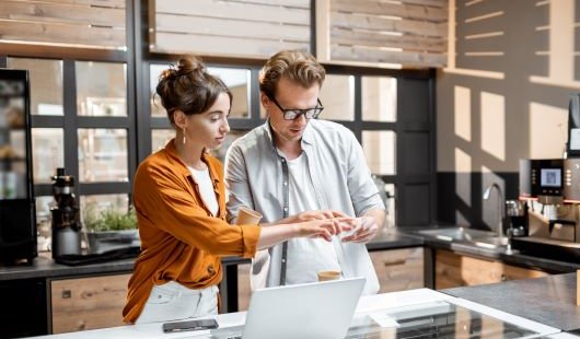 A man and woman in a workplace stand next to a laptop