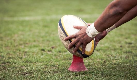Hands holding a rugby ball on a kicking tee. 
