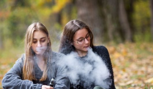 Two young women using vapes outdoors. Image, Adobe.