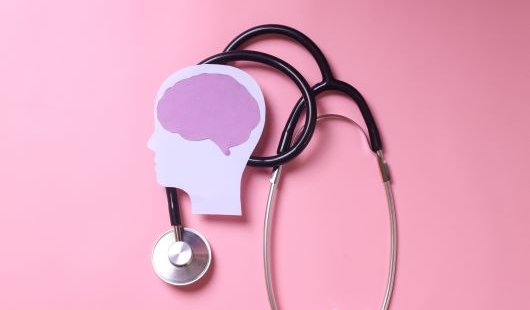 Stethoscope and stylised human head and brain on pink background.