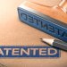 Image: Adobe. A close up of a blue stamp with the word 'patented' stamped on a brown folder.