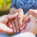 Image: Adobe. A person clasps hands with an elderly person