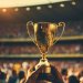 Image: Adobe. A gold trophy being help un in a stadium.