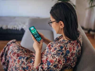 A woman sits on a couch looking at a phone showing a sports betting app