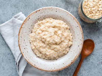 a bowl of porridge sits next to a wooden spoon and a jar of uncooked oats