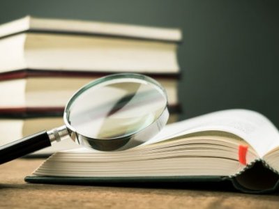 A stack of novels with a magnifying glass.