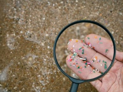 Fingers holding microplastics shown through a magnifying glass