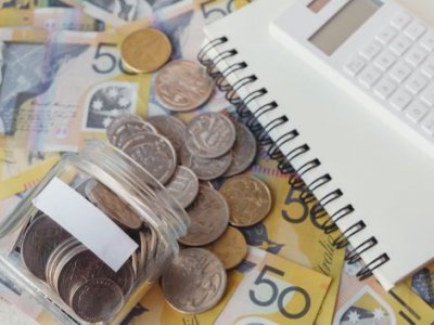 A notebook and calculator sit next to bank notes and a jar of coins
